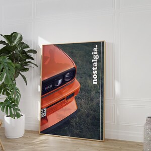 May include: A close-up of the front of an orange BMW M3 car with the word "nostalgia" printed in white on the right side of the image.