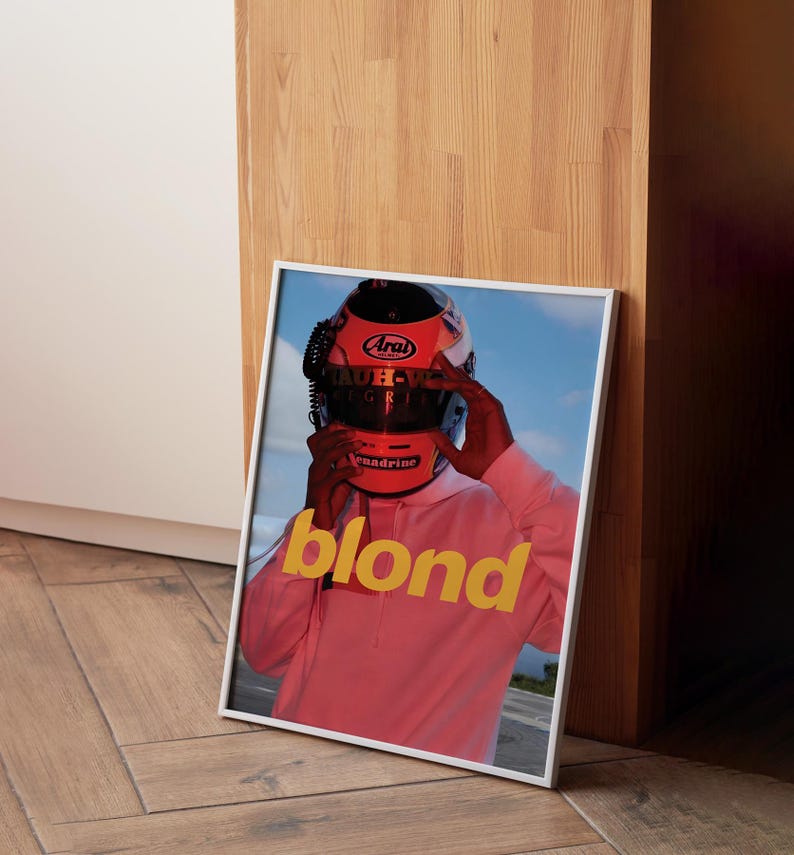 May include: A framed poster featuring a person wearing a red racing helmet and a pink hoodie. The word "blond" is printed in yellow letters on the poster.