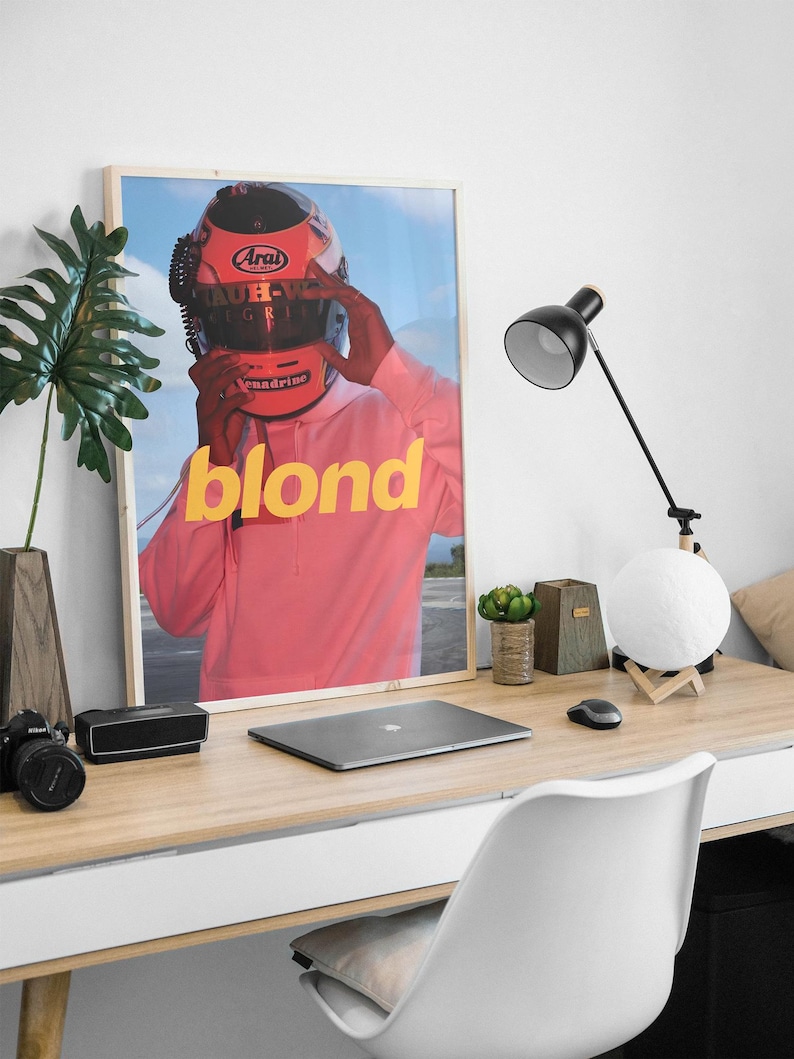 May include: A framed poster featuring a person wearing a red racing helmet with the word "blond" in yellow letters on a pink background.