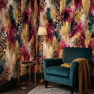 Puede incluir: Un sillón de terciopelo color cerceta con una manta amarilla mostaza, colocado junto a una mesa auxiliar redonda de metal con un libro y una taza. La pared presenta un papel tapiz con un patrón abstracto vertical en tonos oro, magenta y negro.