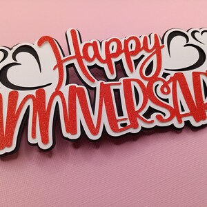 May include: Red and white "Happy Anniversary" cake topper with black outlines and hearts.