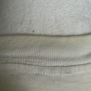 This image showcases a close up view of the yellowing present on the rear collar of a true vintage 1980s salvage condition thrashed Belton Tough Tee women’s 100% preshrunk cotton St. Thomas single stitch graphic t-shirt in a size XL modeled on a dress form.