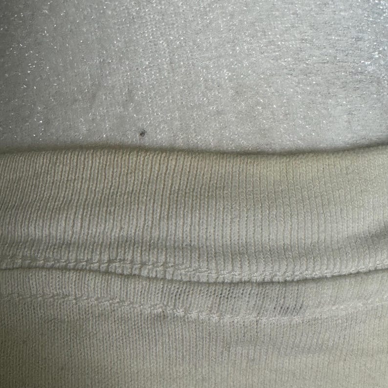 This image showcases a close up view of the yellowing present on the rear collar of a true vintage 1980s salvage condition thrashed Belton Tough Tee women’s 100% preshrunk cotton St. Thomas single stitch graphic t-shirt in a size XL modeled on a dress form.