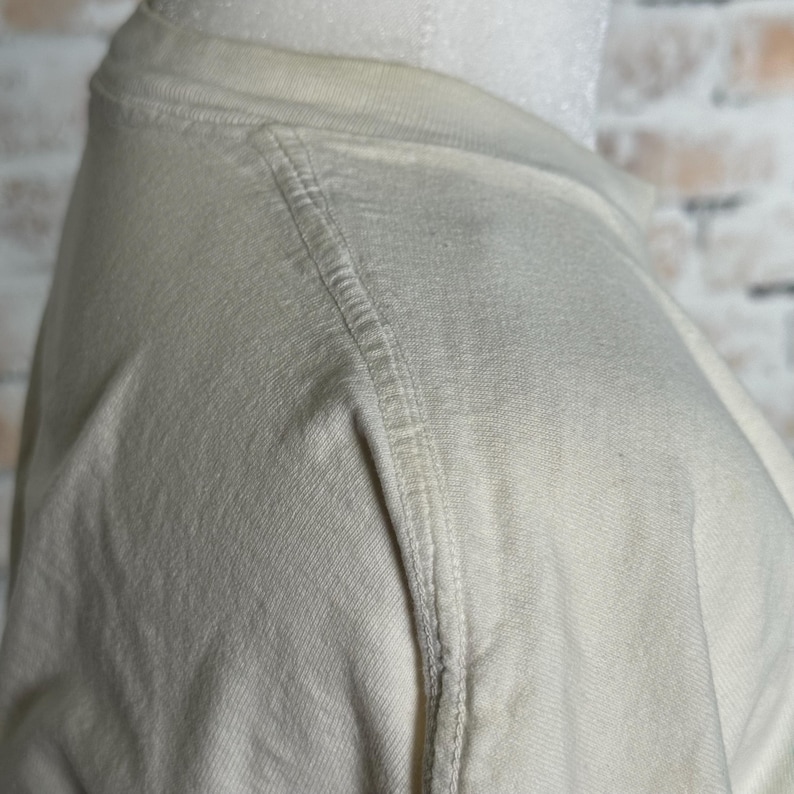 This image showcases the left shoulder of a true vintage 1980s salvage condition thrashed Belton Tough Tee women’s 100% preshrunk cotton St. Thomas single stitch graphic t-shirt in a size XL modeled on a dress form in front of a brick backdrop.
