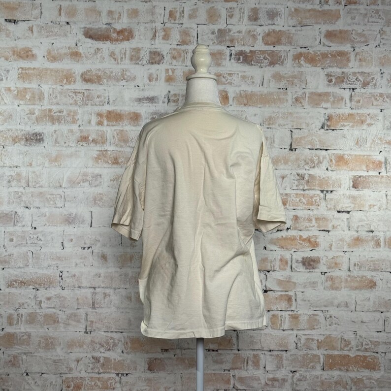 This image showcases the entire back side of a true vintage 1980s salvage condition thrashed Belton Tough Tee women’s 100% preshrunk cotton St. Thomas single stitch graphic t-shirt in a size XL modeled on a dress form in front of a brick backdrop.