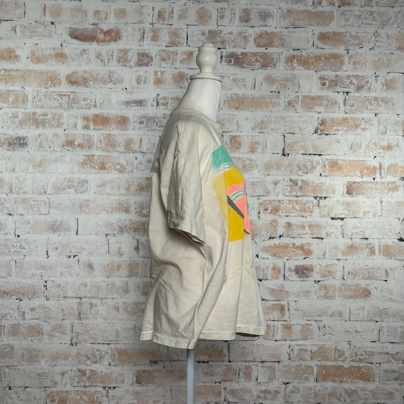 This image showcases the entire left side of a true vintage 1980s salvage condition thrashed Belton Tough Tee women’s 100% preshrunk cotton St. Thomas single stitch graphic t-shirt in a size XL modeled on a dress form in front of a brick backdrop.