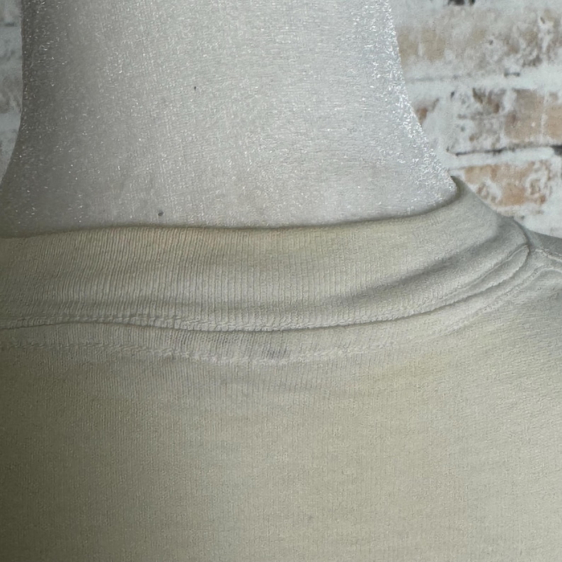 This image showcases the rear collar of a true vintage 1980s salvage condition thrashed Belton Tough Tee women’s 100% preshrunk cotton St. Thomas single stitch graphic t-shirt in a size XL modeled on a dress form in front of a brick backdrop.