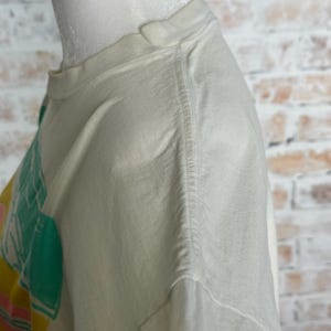 This image showcases the right shoulder of a true vintage 1980s salvage condition thrashed Belton Tough Tee women’s 100% preshrunk cotton St. Thomas single stitch graphic t-shirt in a size XL modeled on a dress form in front of a brick backdrop.