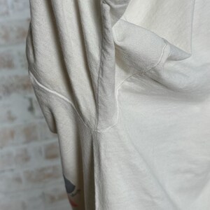 This image showcases the left underarm seam of a true vintage 1980s salvage condition thrashed Belton Tough Tee women’s 100% preshrunk cotton St. Thomas single stitch graphic t-shirt in a size XL modeled on a dress form in front of a brick backdrop.