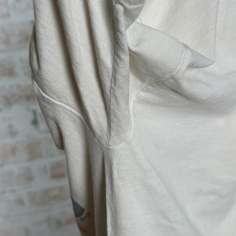 This image showcases the left underarm seam of a true vintage 1980s salvage condition thrashed Belton Tough Tee women’s 100% preshrunk cotton St. Thomas single stitch graphic t-shirt in a size XL modeled on a dress form in front of a brick backdrop.