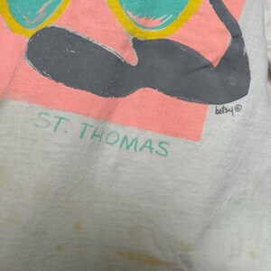 This image showcases a close up view of the logo below the print on the front side of a true vintage 1980s salvage condition thrashed Belton Tough Tee women’s 100% preshrunk cotton St. Thomas single stitch graphic t-shirt in a size XL modeled on a dress form.