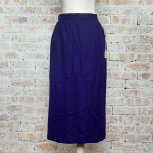 May include: A solid, dark purple skirt with a straight, knee-length cut. The skirt has a high waist and a simple, classic design. A tag is attached to the side. The skirt is displayed on a mannequin against a brick wall background.