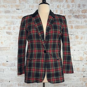May include: A plaid blazer in a classic pattern of red, green, and yellow on a black background. The blazer has a black velvet collar, a single-button closure, and two front pockets. The garment is displayed on a mannequin.