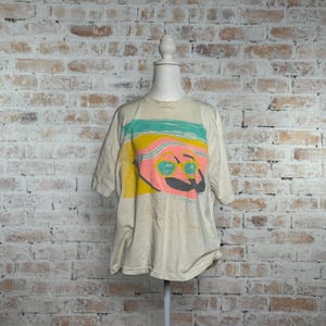 This image showcases the entire front side of a true vintage 1980s salvage condition thrashed Belton Tough Tee women’s 100% preshrunk cotton St. Thomas single stitch graphic t-shirt in a size XL modeled on a dress form in front of a brick backdrop.
