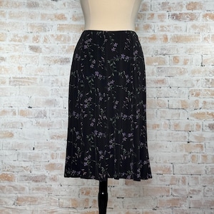 May include: Black midi skirt with a floral pattern. The skirt features a dark background with a repeating pattern of small purple flowers and green leaves. The skirt is displayed on a mannequin.