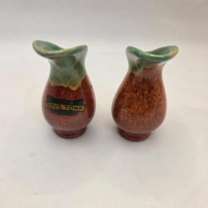 May include: Two small, ceramic vases with a speckled brown finish and a green rim. Each vase has a label that reads "Souvenir of Boys Town Nebraska". The vases have a unique, curved opening.