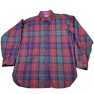 May include: A long-sleeve button-down shirt featuring a plaid pattern in shades of maroon, dark green, and navy blue. The shirt includes a pointed collar, a single chest pocket on the left side, and buttons along the front placket and cuffs.