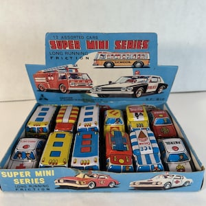 Può includere: Un set di giocattoli vintage con 12 mini auto assortite in una scatola di cartone blu. La scatola riporta "SUPER MINI SERIES" e "LONG RUNNING FRICTION". Le auto includono un autobus scolastico, un'autopompa, un'auto della polizia e un'ambulanza.