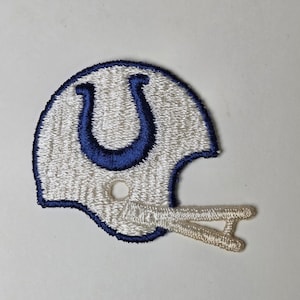 May include: Embroidered patch featuring a white football helmet with a blue horseshoe logo. The helmet has a blue outline and a tan face mask. The patch is likely for a sports fan or collector.