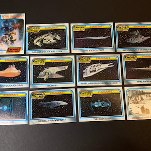May include: A collection of vintage Star Wars trading cards featuring various spacecraft and scenes from the movie "The Empire Strikes Back." The cards have a blue border and include images of the Millennium Falcon, TIE Fighter, and more.