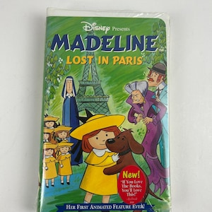 May include: A sealed VHS tape of Disney's "Madeline: Lost in Paris." The cover features a cartoon illustration of Madeline in a yellow dress and hat, with a brown dog, and other characters in front of the Eiffel Tower. The tape is in a plastic wrap.