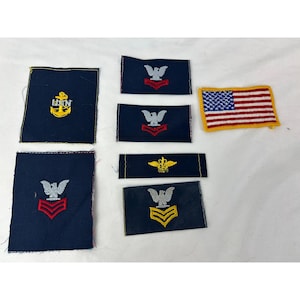 Puede incluir: Un conjunto de parches bordados en azul marino y amarillo, incluyendo un parche de la bandera estadounidense. Los parches presentan varios emblemas, como una ancla, un águila y galones, probablemente insignias militares.