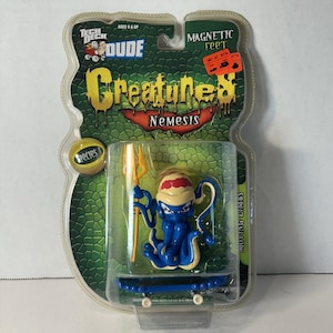 May include: A blue and yellow Tech Deck Creatures Nemesis fingerboard toy with a blue and white skateboard and a trident. The packaging has the words "Tech Deck Dude" and "Magnetic Feet" on it.