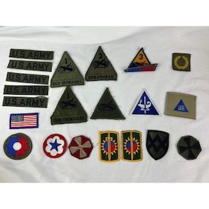 May include: A collection of various military patches and insignias. Includes rectangular patches with "U.S. ARMY" text, triangular patches with unit designations, and circular and shield-shaped patches. Colors include green, blue, red, and gold.