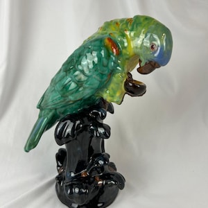 May include: A ceramic parrot figurine in shades of green, yellow, and blue, perched on a black base. The parrot has a detailed, glossy finish with red accents. The figurine is a decorative item.