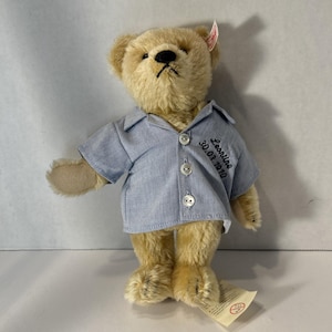May include: A light brown teddy bear wearing a blue button-up shirt with the name Leonline and the date 30.01.2010 embroidered on it.