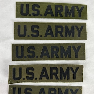 May include: Five olive green fabric patches with the text "U.S. ARMY" in black block letters. The patches are rectangular and appear to be embroidered or woven. They are arranged vertically on a white background.