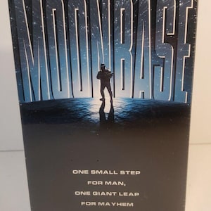 May include: A black box featuring the word "MOONBASE" in large, blue, stylized letters. A silhouetted figure stands in front of the word. The text "ONE SMALL STEP FOR MAN, ONE GIANT LEAP FOR MAYHEM" is below.