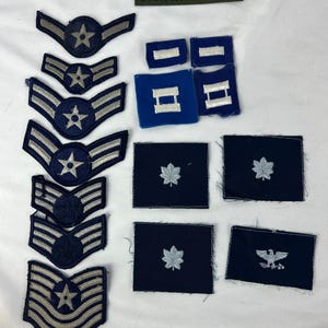 May include: A collection of U.S. Air Force patches and insignia. Includes various rank insignia, wing emblems with stars, and a green rectangular patch with the text "U.S. AIR FORCE". The patches are in shades of blue, silver, and green.