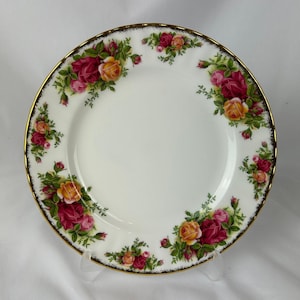 以下が含まれることがあります： 金色の縁と、赤、ピンク、黄色のバラの花柄が施された白いセラミックプレート。 プレートには装飾的なボーダーがあり、食品の提供に適しています。