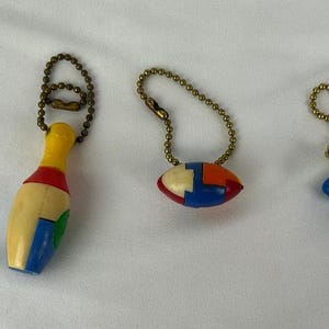 Puede incluir: Una colección de llaveros coloridos con diseños temáticos deportivos. Incluye un jugador de béisbol, un bolo, dos balones de fútbol americano y una pelota. Cada llavero tiene una cadena de metal y un cierre para sujetar a llaves o bolsos.