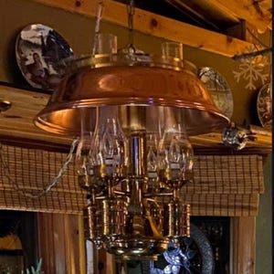 Può includere: Un lampadario vintage in ottone e rame con più paralumi in vetro. Il lampadario ha un grande paralume svasato in rame ed è sospeso al soffitto. Piatti decorativi sono visibili sullo sfondo.
