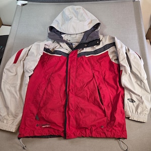 May include: A red and tan Columbia winter jacket with a hood. The jacket has a black and gray trim, a zipper closure, and the Columbia logo on the chest and sleeve. The jacket is designed for outdoor activities.