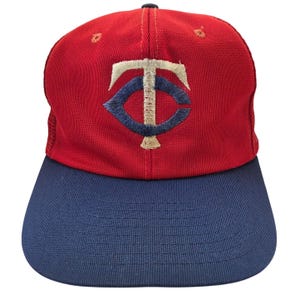 Könnte beinhalten: Rote und marineblaue Baseballkappe mit dem gestickten Logo der Minnesota Twins. Die Kappe hat eine rote Krone und einen marineblauen Schirm. Das Logo ist weiß, marineblau und beige.