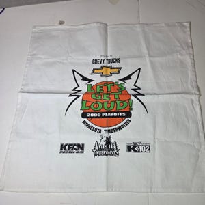 May include: White towel featuring a basketball design with the text "LET'S GET LOUD! 2000 PLAYOFFS" and the Minnesota Timberwolves logo. The towel also includes the Chevy Trucks logo and radio station logos.