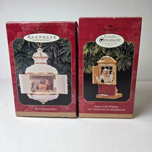May include: Two Hallmark Keepsake Christmas ornaments in their original boxes. One depicts the Nativity scene, the other a man looking out a window. The boxes are red with green accents and the words "Keepsake Ornament" are visible.