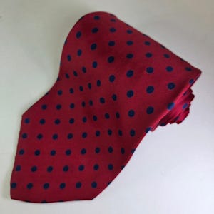 May include: A red tie featuring a pattern of navy blue polka dots. The tie is folded over, revealing both sides of the fabric. The material appears to be smooth and the tie is a classic accessory.