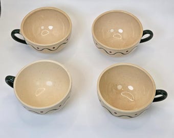 May include: Four beige ceramic soup bowls with dark green handles. Each bowl has a wavy green line with small red dots around the rim. The bowls are arranged in a square on a white surface.