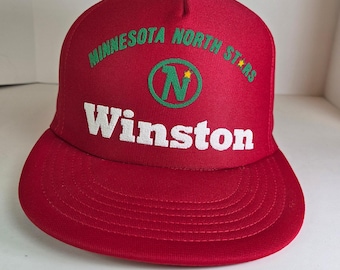 May include: A red baseball cap with a flat brim. The cap displays the text "MINNESOTA NORTH STARS" in green above a green circle with a white "N" and a star. The name "Winston" is printed in white below.
