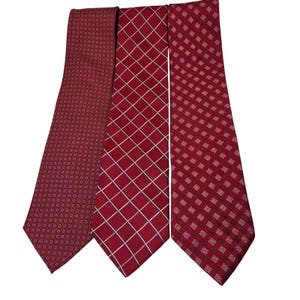 May include: Three red neckties with different patterns. The tie on the left has a repeating small circle pattern. The middle tie has a white grid pattern. The tie on the right has a repeating small square pattern.