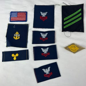 Puede incluir: Una colección de parches e insignias militares vintage. Incluye un pequeño parche de la bandera estadounidense, parches azul marino con diseños de águilas y galones, un parche con rayas verdes y un parche dorado.