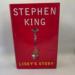 May include: A hardcover book titled Lisey's Story by Stephen King. The cover is bright red with white text for the author's name and yellow text for the title. A shovel-shaped cutout in the center reveals a colorful floral pattern underneath.