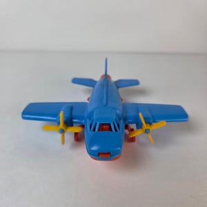 May include: A blue toy airplane with yellow propellers and red accents. The toy plane has a classic design with wings and a tail. The propellers are yellow, and the nose and other details are red.