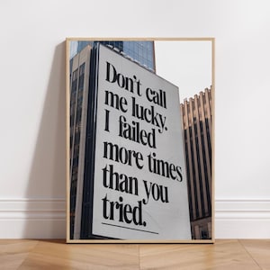 May include: A black and white motivational quote on a building in a city. The quote reads "Don't call me lucky. I failed more times than you tried."