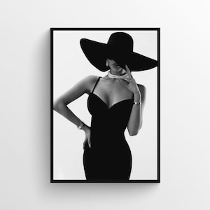 Puede incluir: Una fotografía en blanco y negro de una mujer con un vestido negro y un gran sombrero negro. Ella está mirando hacia abajo y tocándose la cara con la mano.