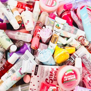 May include: A selection of lip balms, lip scrubs and lip glosses in a range of colours and flavours. The lip balms are in tubes, jars and sticks. The lip scrubs are in jars. The lip glosses are in tubes. The lip balms and lip scrubs have a variety of designs and patterns. The lip glosses are clear, pink and red. The lip balms and lip scrubs are in a variety of colours, including pink, red, blue, green and yellow.